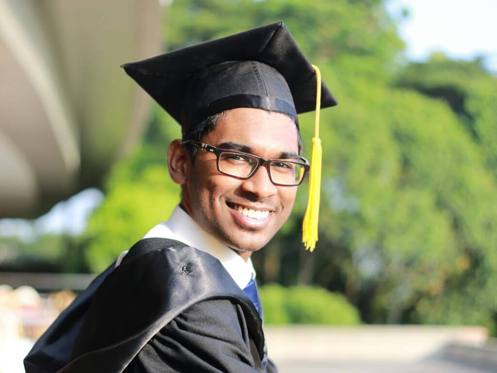 A young graduate in a cap and gown, smiling outdoors.