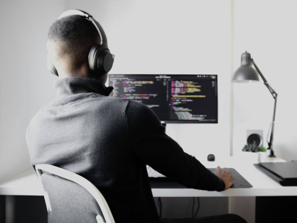 A man wearing headphones, working on a computer with code on the screen, representing IT and cybersecurity employment.