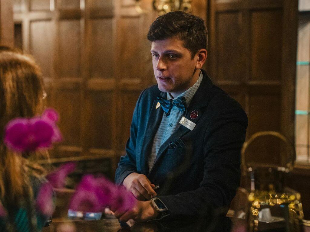 A hotel concierge or customer service representative wearing a bow tie, assisting a guest.