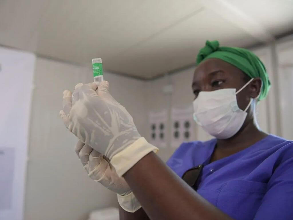 A healthcare worker in gloves and a mask, preparing a syringe.