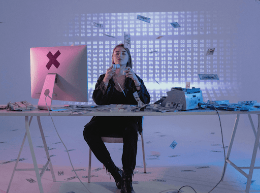Young female sitting a a desk with a computer to her left and money calculator to her right with money stakes on the table and in air.