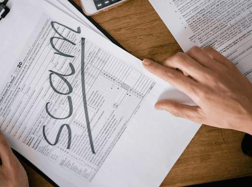 Hand holding professional documents that having the words scam written across the page.