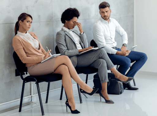 Three professional-looking people sitting in chairs waiting, they are all holding a document.