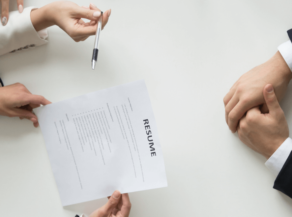 A close-up of a CV being discussed across a white desk during an interview.