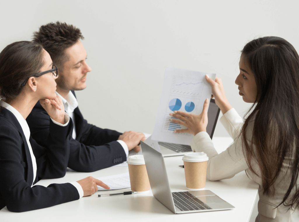 A professional woman presenting a report with charts to two representatives during a job interview. The interviewers are listening attentively.