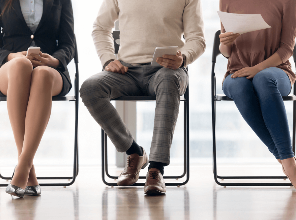 Three job candidates sitting in a row, holding documents and devices while waiting for an interview.