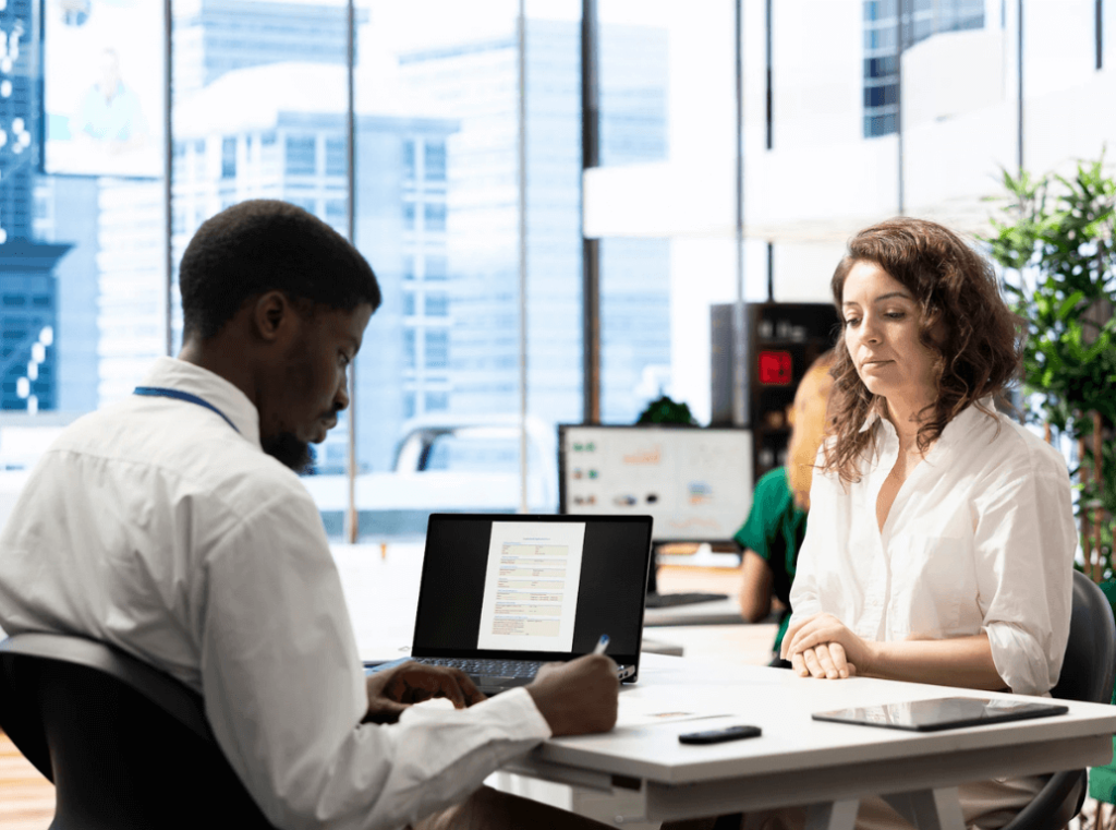 Employer conducting a job interview while reviewing a candidate’s application on a laptop.