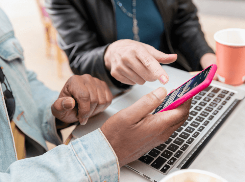 Two colleagues looking at a smartphone screen and a laptop together.