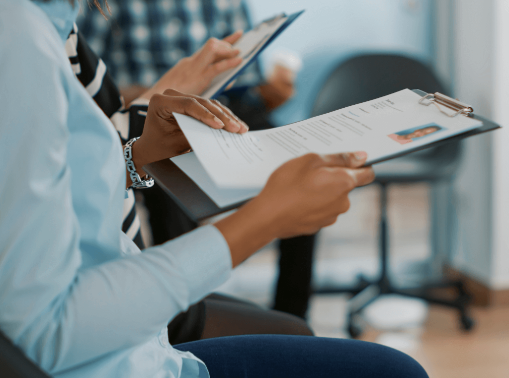 Close-up of a candidate’s hands holding a clipboard and flipping through recruitment documents while waiting for an interview.