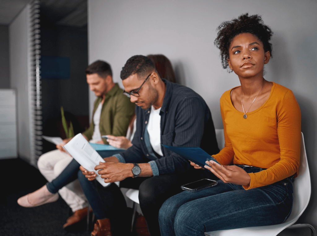 A group of job applicants sitting in a waiting room with their CVs, preparing for their interviews.