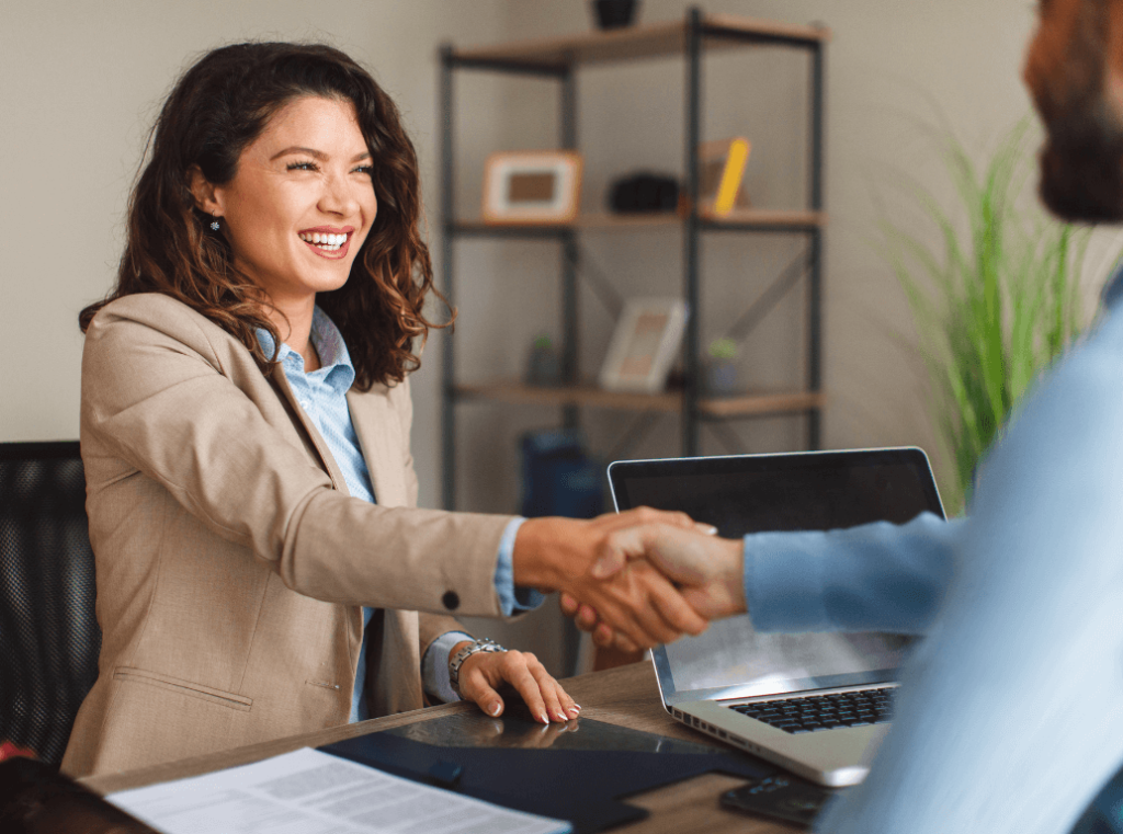 A smiling female candidate shaking hands with an interviewer across a desk.