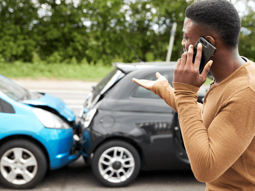 Frustrated man talking on his phone in front of a car crash, highlighting the importance of driver licence verification for fleet safety.