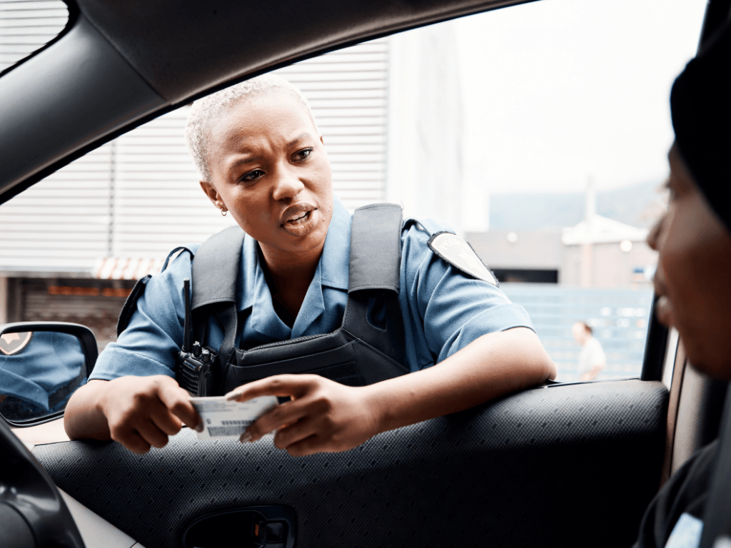 A police officer speaking with a driver through an open car window, conducting routine licence verification.